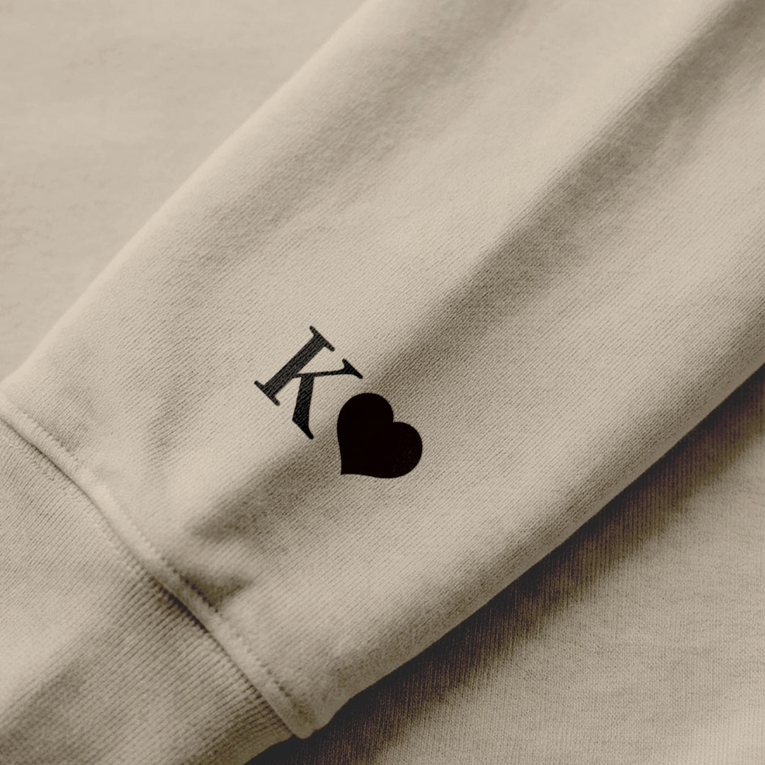 Nahaufnahme Ärmeldruck: Initiale mit Herz auf sandfarbenem Hoodie