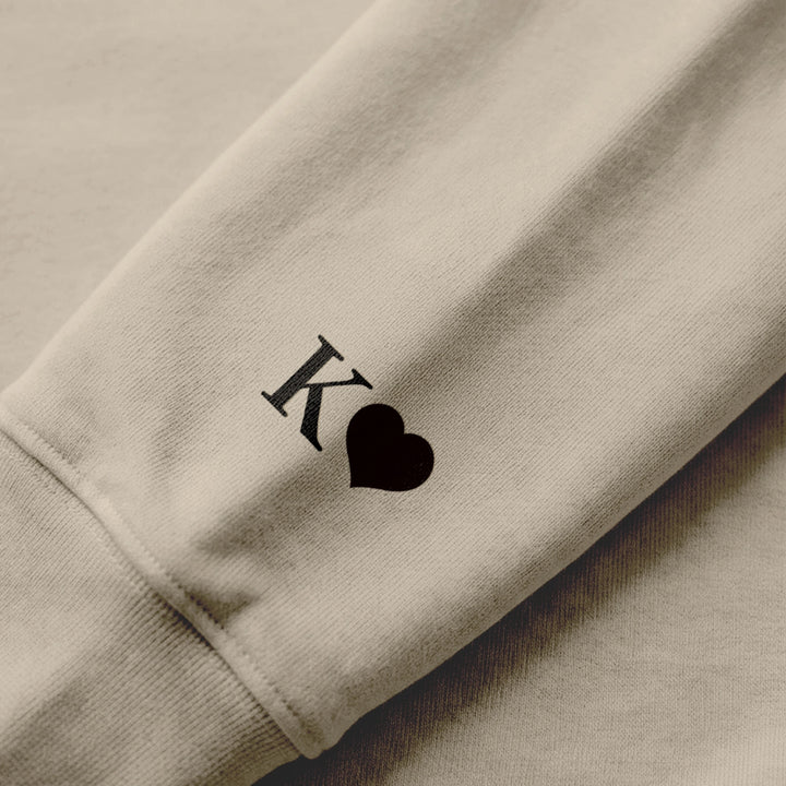Nahaufnahme Ärmeldruck: Initiale mit Herz auf sandfarbenem Hoodie