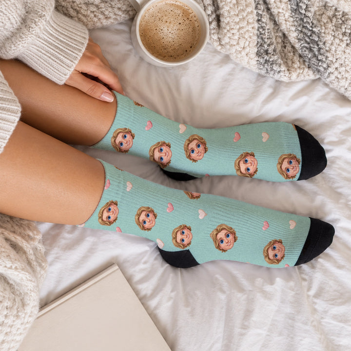 Mintgrüne Socken mit Comic-Kopf und Herzen, gemütlich getragen im Bett