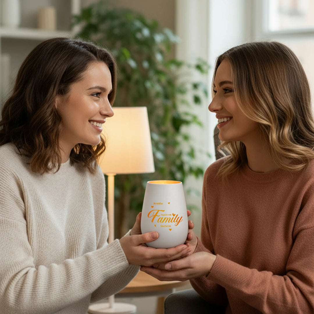Zwei Freundinnen halten gemeinsam das weiße Windlicht „Friends are Family“