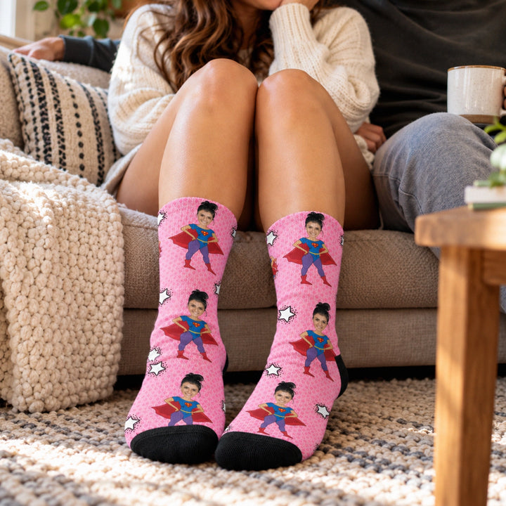 Frau auf dem Sofa trägt rosa Superheldin-Socken mit ihrem Gesicht