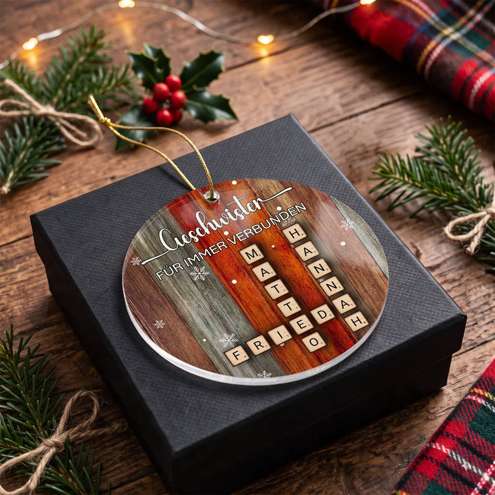 Weihnachtsbaumschmuck „Geschwister“ mit vier Namen als Scrabble-Steine auf einer schwarzen Geschenkbox