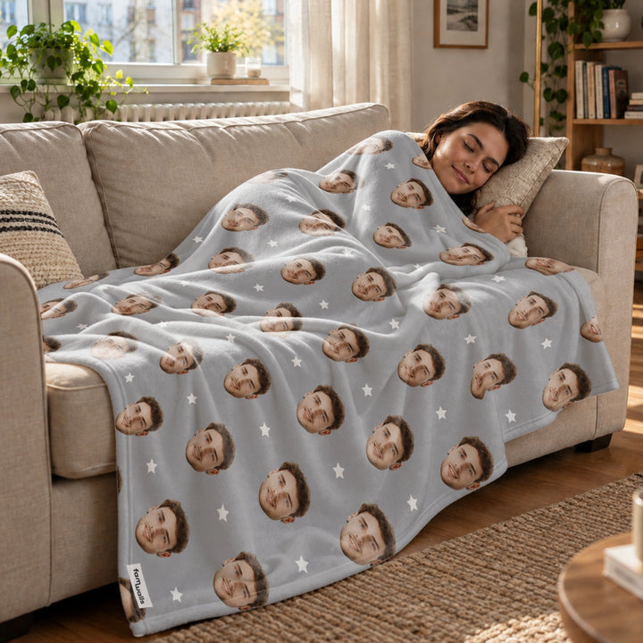 Frau schläft auf dem Sofa unter der grauen Foto-Decke mit Gesichtern und Sternen