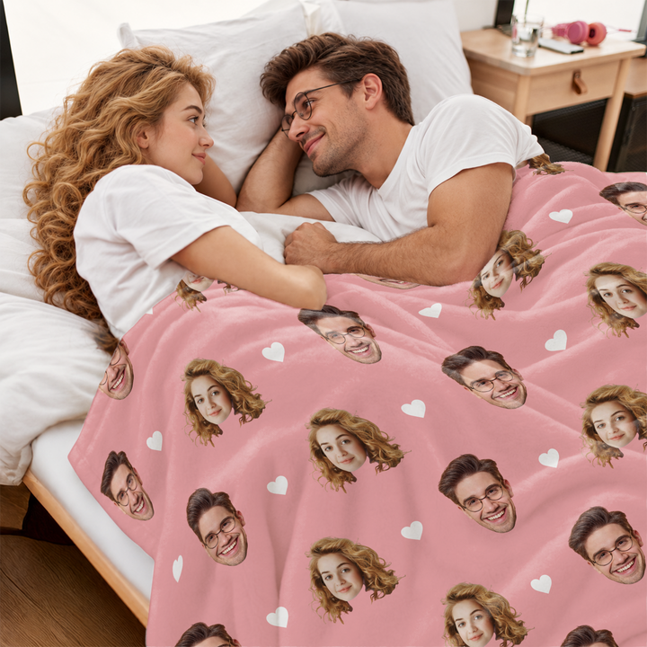 Paar liegt im Bett unter der rosa Foto-Decke mit aufgedruckten Gesichtern