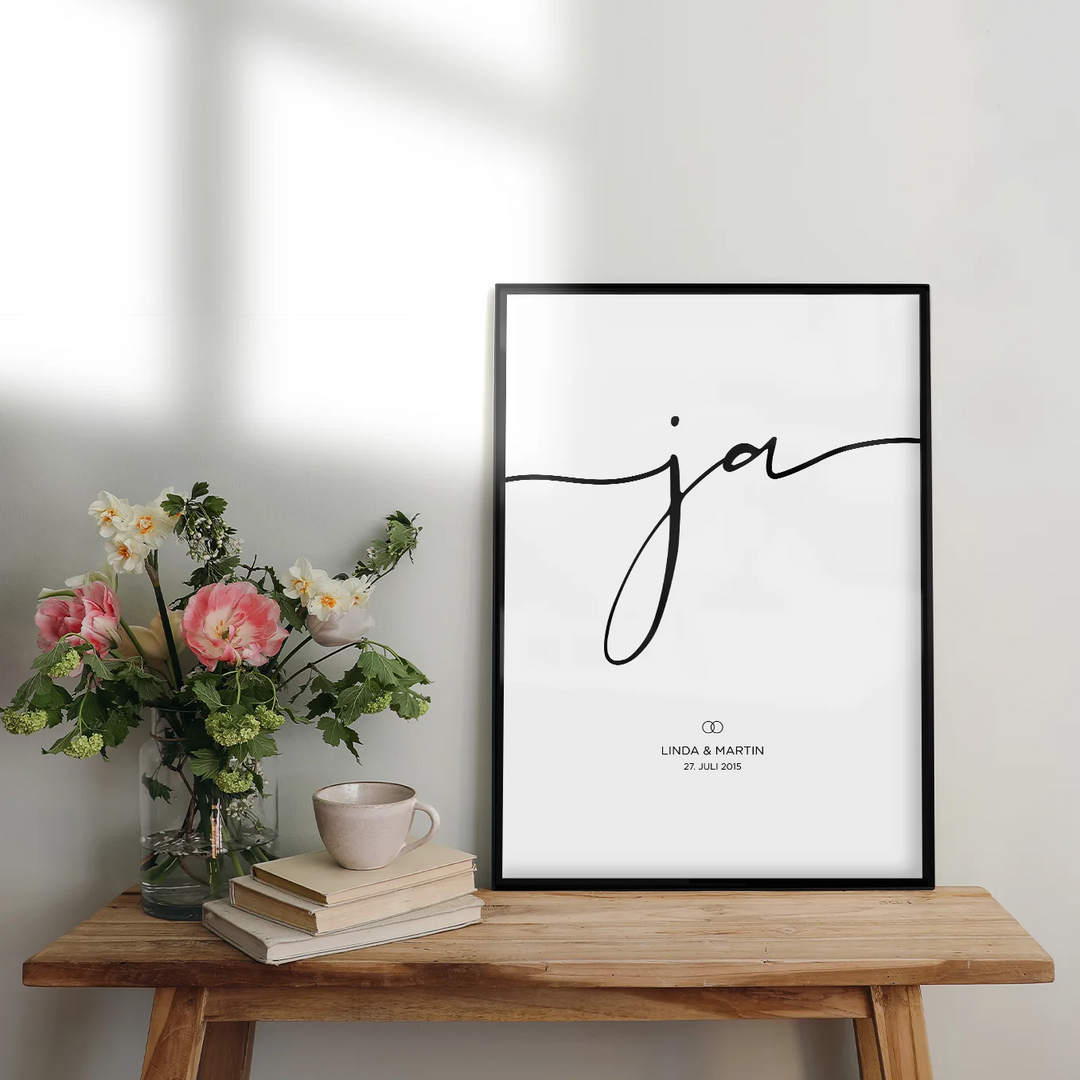 Personalisiertes Hochzeitsposter mit eleganter "Ja" Schrift, gerahmt auf Holztisch neben Blumenstrauß, Büchern und Tasse, perfektes Hochzeitsgeschenk für Linda und Martin