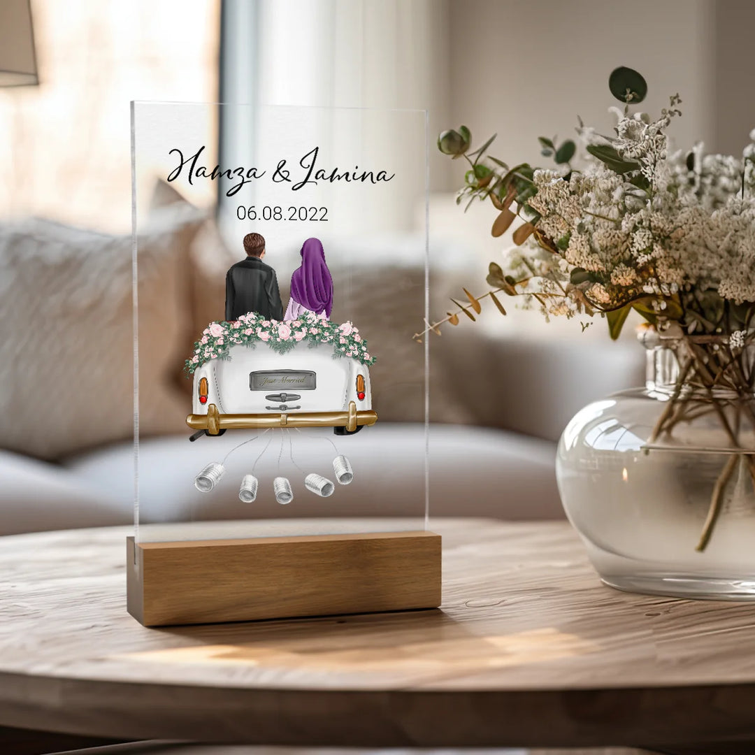 Personalisierte Acryltafel als Hochzeitsgeschenk mit muslimischem Brautpaar auf Auto, Namen und Datum, neben Blumenvase auf Holztisch. Elegantes Geldgeschenk für "Just Married" Paar.