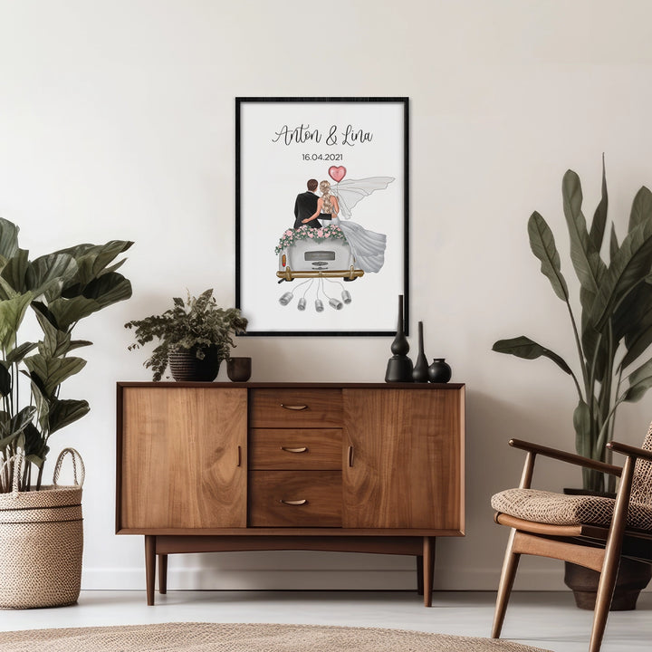 Personalisiertes Hochzeitsposter "Just Married" in schwarzem Rahmen auf Kommode, umgeben von Zimmerpflanzen. Illustration zeigt Brautpaar im Auto mit Geldscheinen. Ideales Geldgeschenk für Hochzeiten.